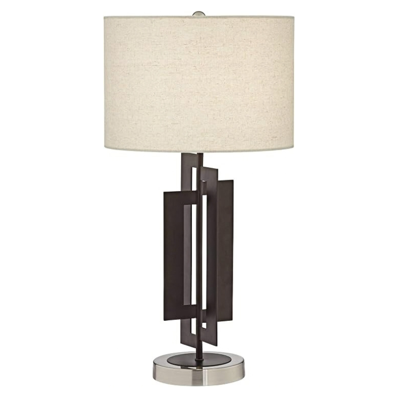 A modern table lamp with a cylindrical beige fabric shade, a dark bronze geometric metal base, and a polished silver circular base, shown against a plain white background.