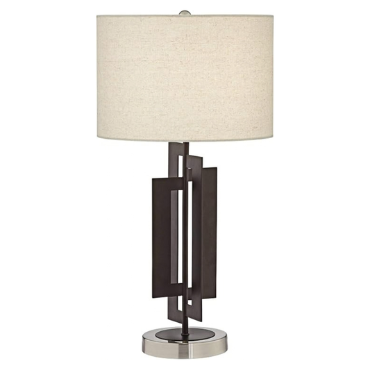 A modern table lamp with a cylindrical beige fabric shade, a dark bronze geometric metal base, and a polished silver circular base, shown against a plain white background.